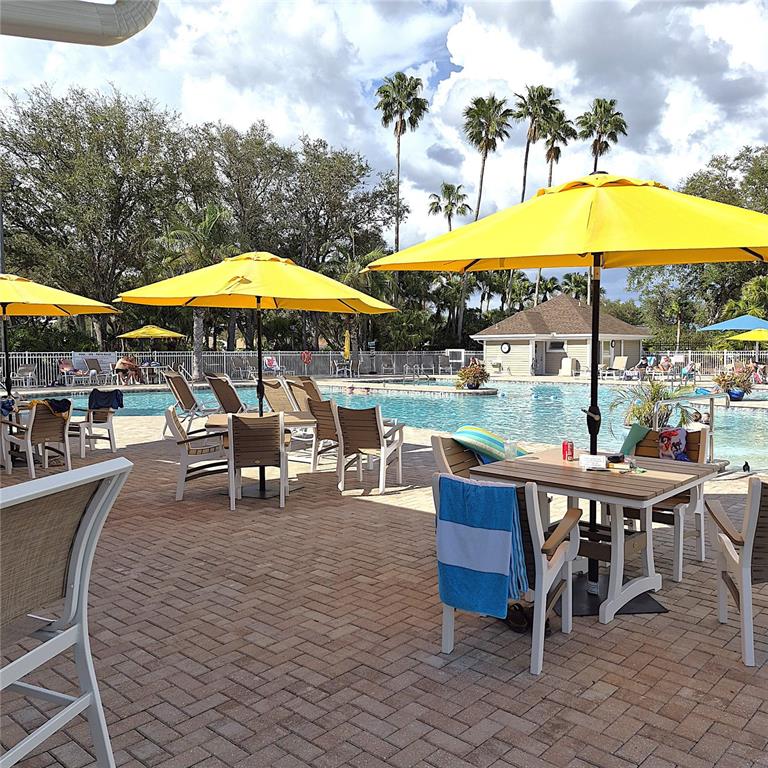 A paved pool deck features several tables with yellow umbrellas and chairs near a swimming pool — 14016 WILLOW GLEN COURT UNIT 212, PORT CHARLOTTE, FL