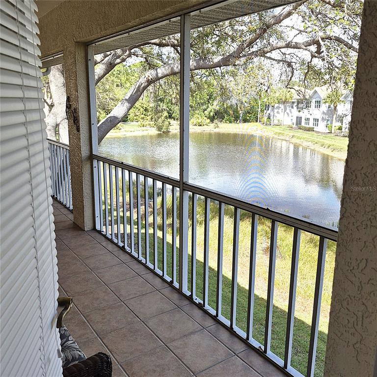 A screened-in balcony with tiled flooring overlooks a pond and nearby residential buildings — 14016 WILLOW GLEN COURT UNIT 212, PORT CHARLOTTE, FL