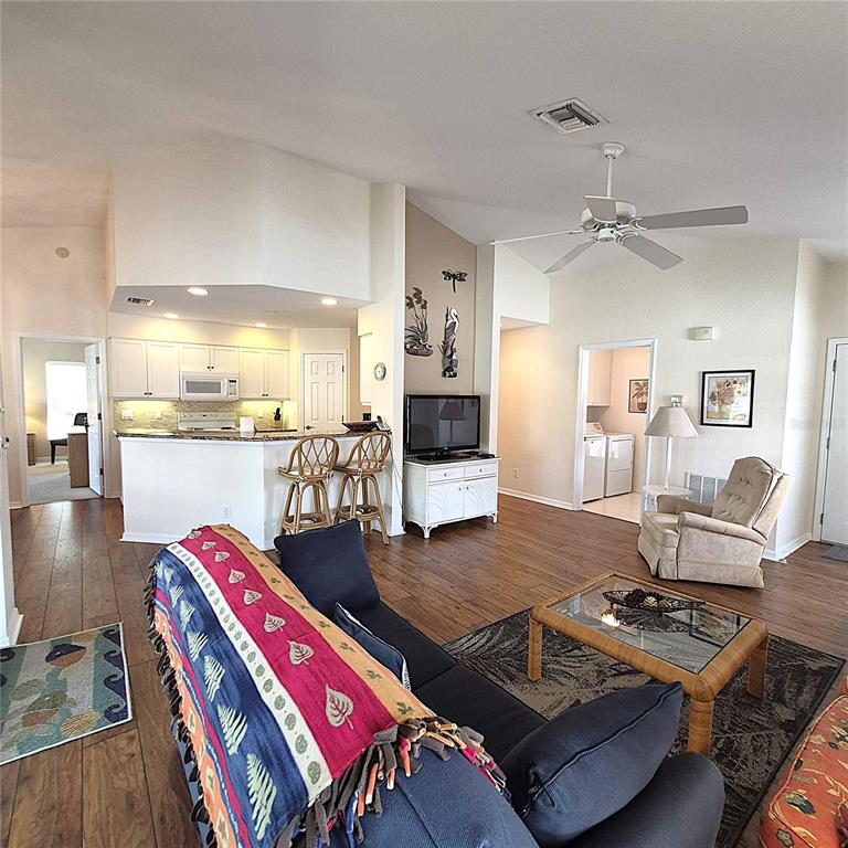A living room with wood-look flooring, a kitchen island with bar stools, and a ceiling fan — 14016 WILLOW GLEN COURT UNIT 212, PORT CHARLOTTE, FL