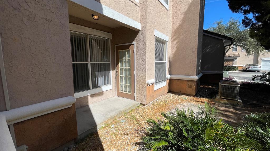 A tan stucco building exterior features a glass-paned door, windows, and a gravel patio area — 17954 VILLA CREEK DRIVE UNIT 17954, TAMPA, FL