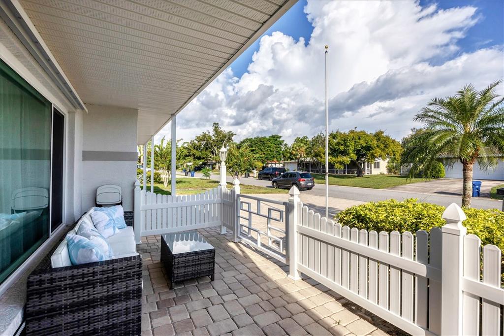 A covered patio with a wicker sofa, glass-top table, and white vinyl fencing overlooks a street — 3126 BOUGAINVILLEA STREET, SARASOTA, FL