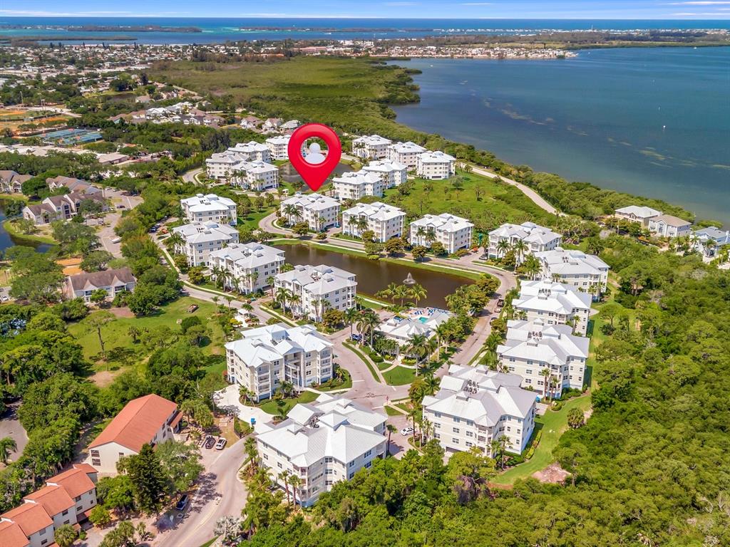 An aerial view shows a residential complex with white buildings surrounding a central pond — 7840 34TH AVENUE W UNIT 202, BRADENTON, FL