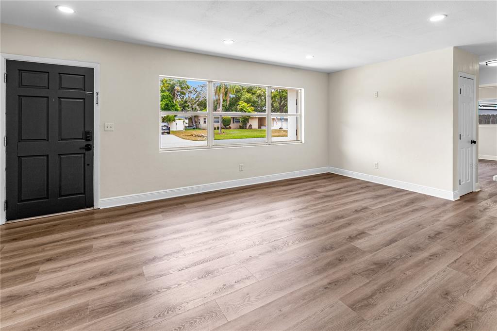 A living room with light-colored walls, wood-look flooring, a large window, and a black door — 12120 CROFT DRIVE, LARGO, FL