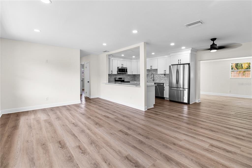 A bright, open-concept living area features light wood-look flooring and a kitchen with white cabinets — 12120 CROFT DRIVE, LARGO, FL