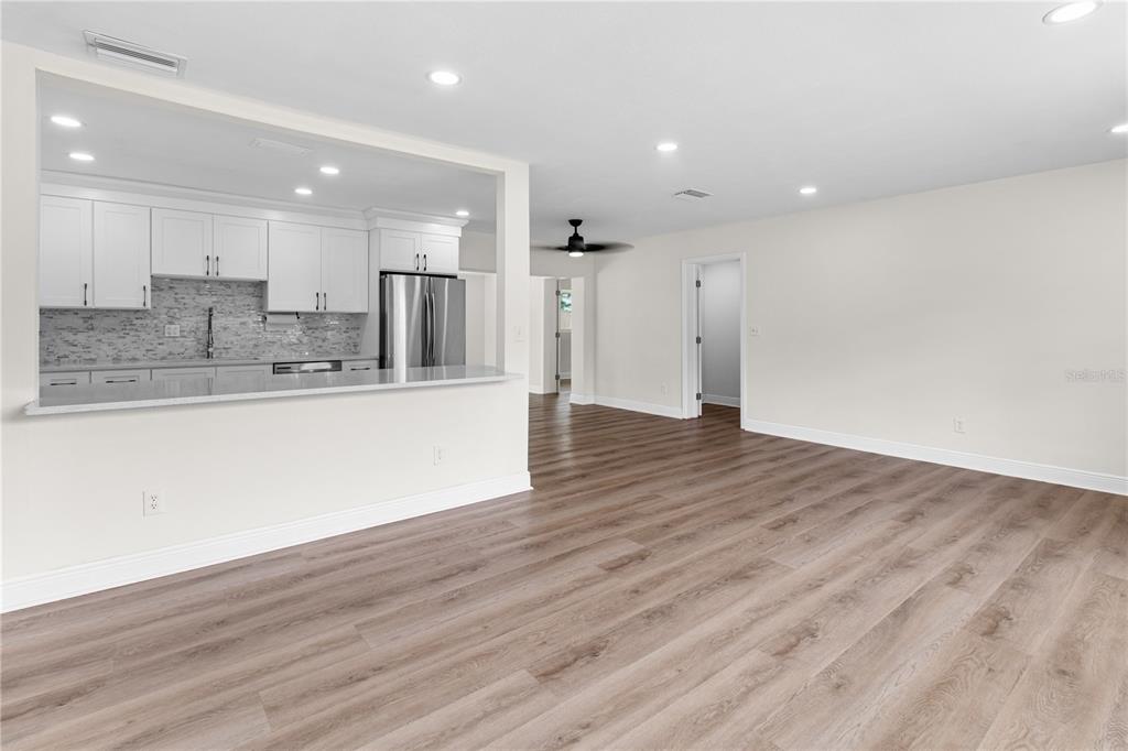 A bright, open-concept living area features light wood-look flooring and a kitchen with white cabinets — 12120 CROFT DRIVE, LARGO, FL