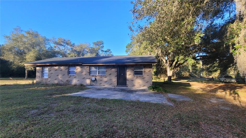 A single-story brick house with a concrete patio sits on a grassy lot with trees — 883 W OHIO AVENUE, LAKE HELEN, FL
