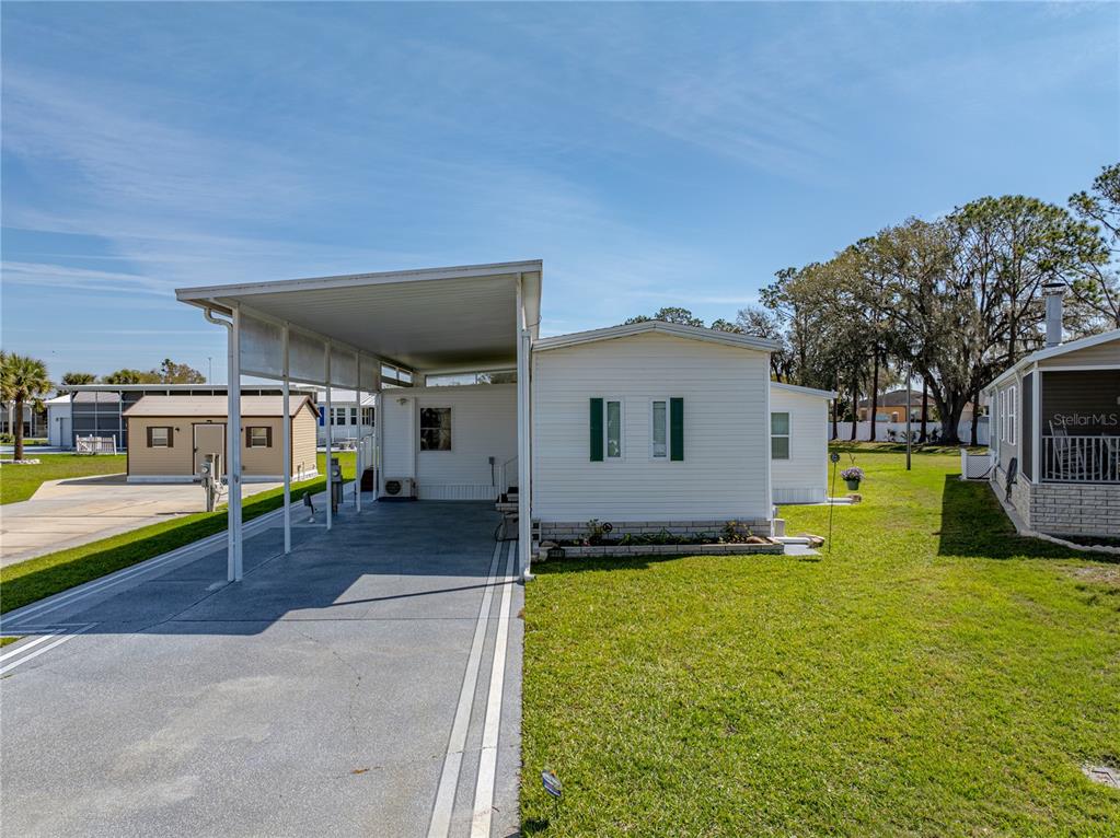 A single-story manufactured home with a carport and a small shed in the background — 8925 SOUTHSHORE COURT, POLK CITY, FL