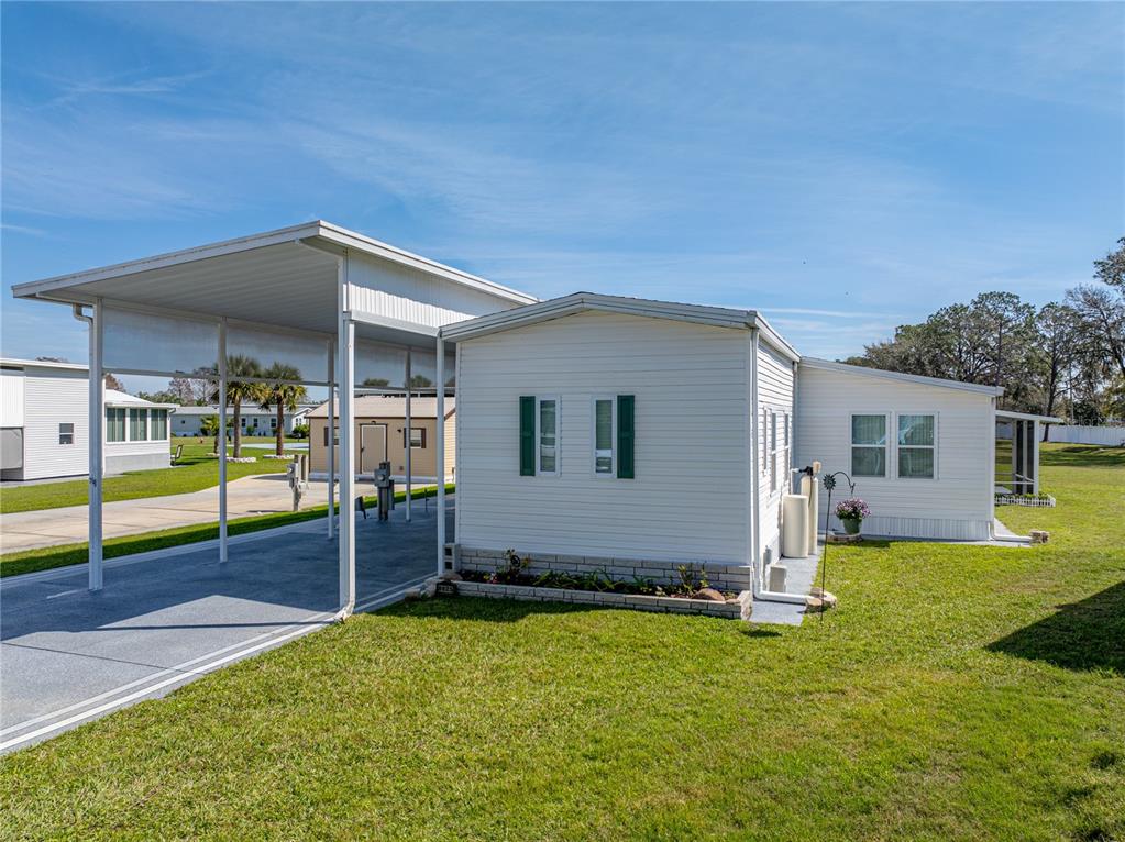A white mobile home with a metal carport and a small brick-bordered garden bed — 8925 SOUTHSHORE COURT, POLK CITY, FL