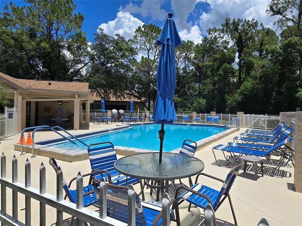 A swimming pool with lounge chairs and a patio table under a blue umbrella — 6695 PIN OAK COURT, SPRING HILL, FL