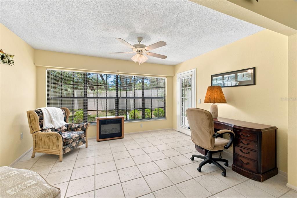 A sunlit home office features tile flooring, a desk, a wicker chair, and a ceiling fan — 6695 PIN OAK COURT, SPRING HILL, FL