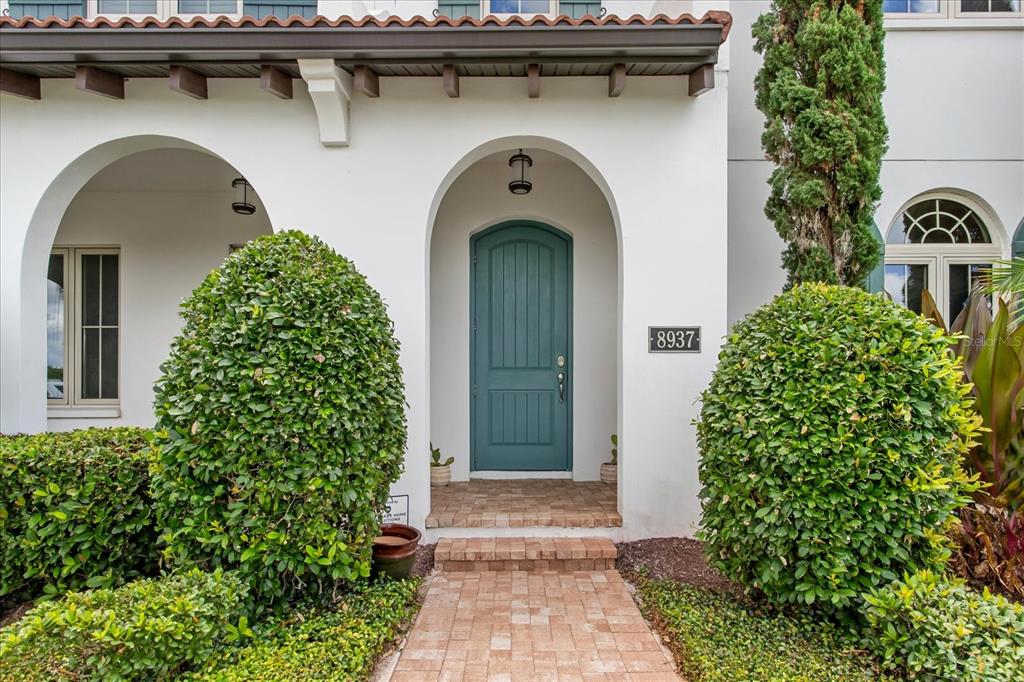 A teal arched front door is centered between two large shrubs and a brick walkway — 8937 LAKESHORE POINTE DRIVE, WINTER GARDEN, FL