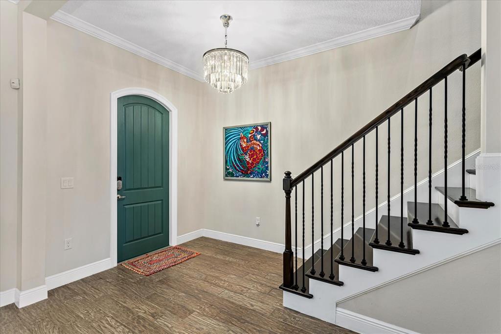 An entryway features a green arched door, a crystal chandelier, and a dark wood staircase — 8937 LAKESHORE POINTE DRIVE, WINTER GARDEN, FL
