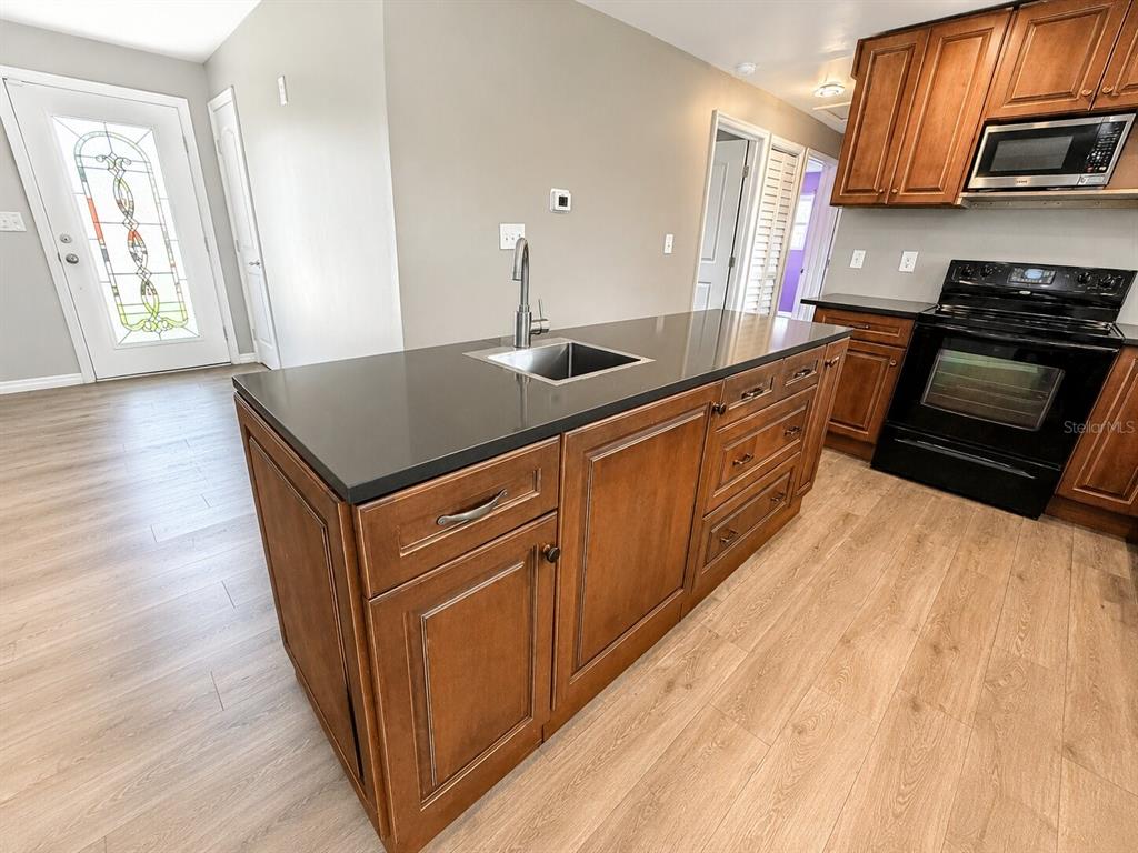 A kitchen island with a sink and dark countertops sits in a room with wood flooring — 53 HIGHRIDGE ROAD, DAYTONA BEACH, FL