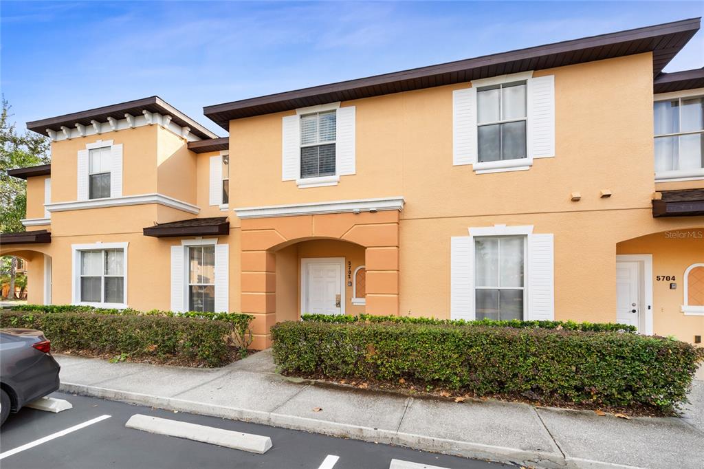 A two-story peach-colored apartment building with white shutters and a hedge-lined sidewalk — 5702 DELOREAN DRIVE, KISSIMMEE, FL