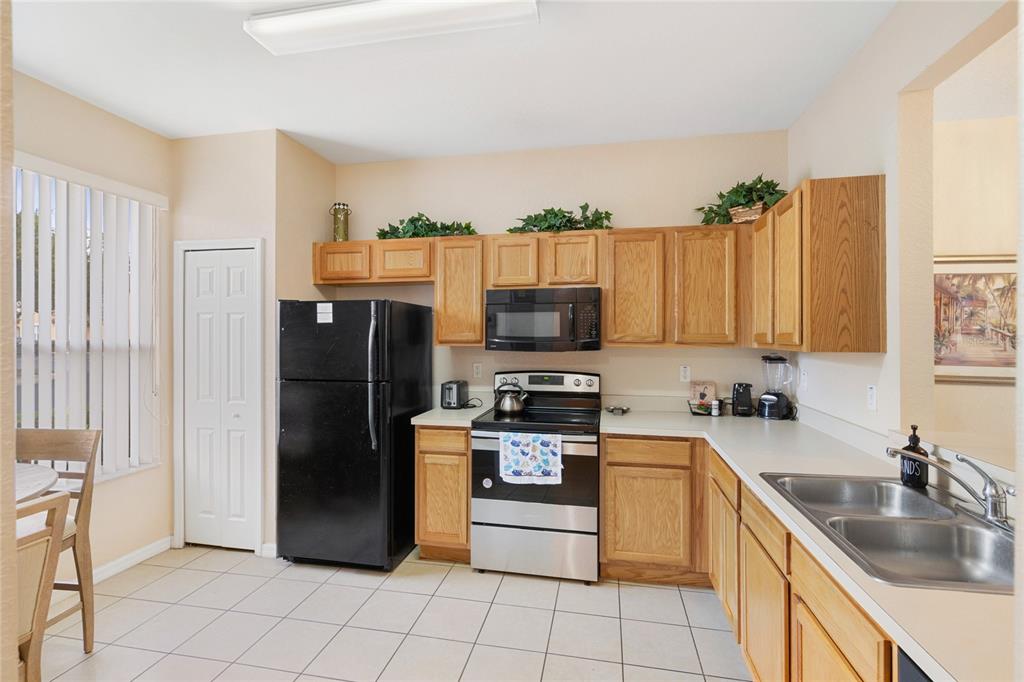 A kitchen features oak cabinets, black appliances, a stainless steel stove, and light tile flooring — 5702 DELOREAN DRIVE, KISSIMMEE, FL