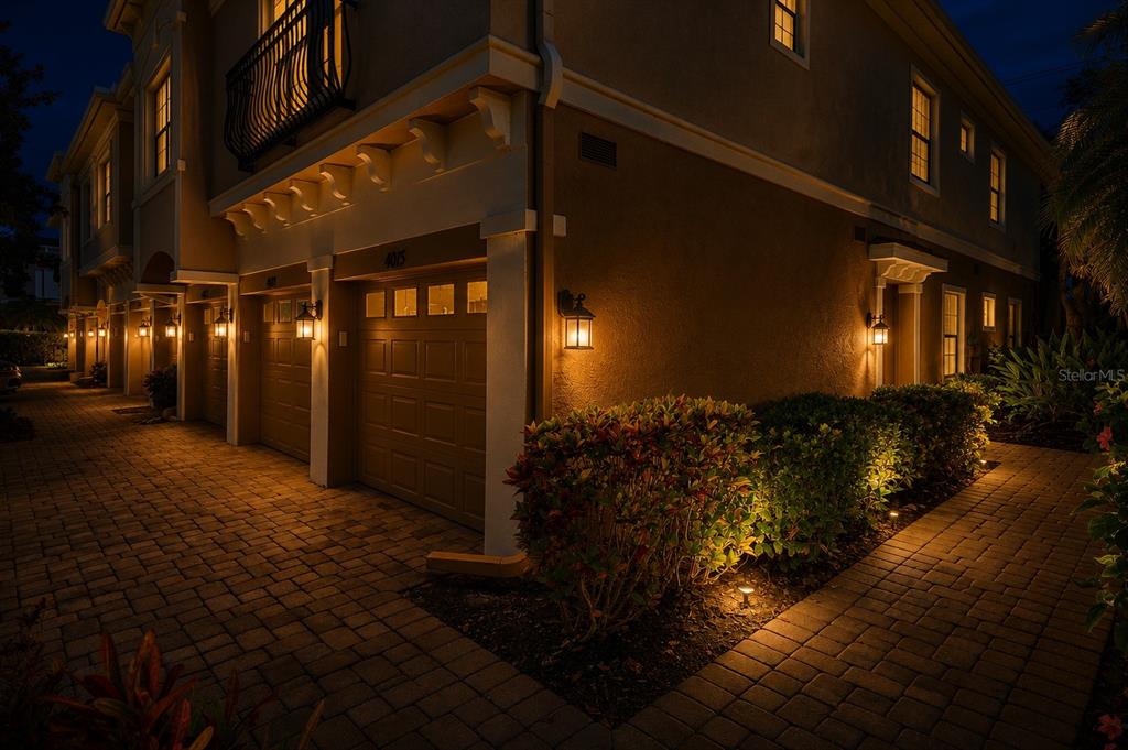 Exterior view of a multi-unit townhouse building at night with lit garage doors and landscaping — 4015 OVERTURE CIRCLE UNIT 312, BRADENTON, FL