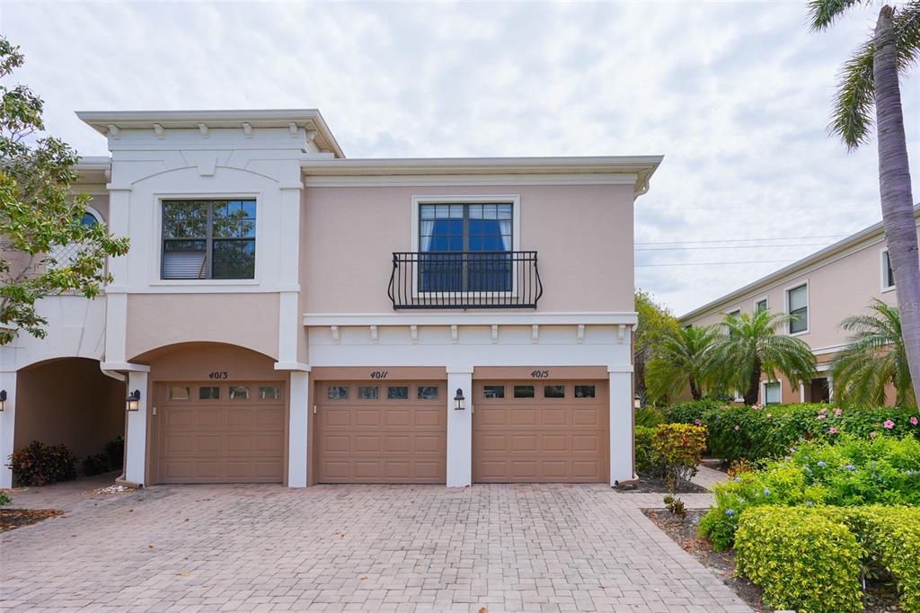 A two-story townhouse exterior features three garage doors, a balcony, and a paved driveway — 4015 OVERTURE CIRCLE UNIT 312, BRADENTON, FL