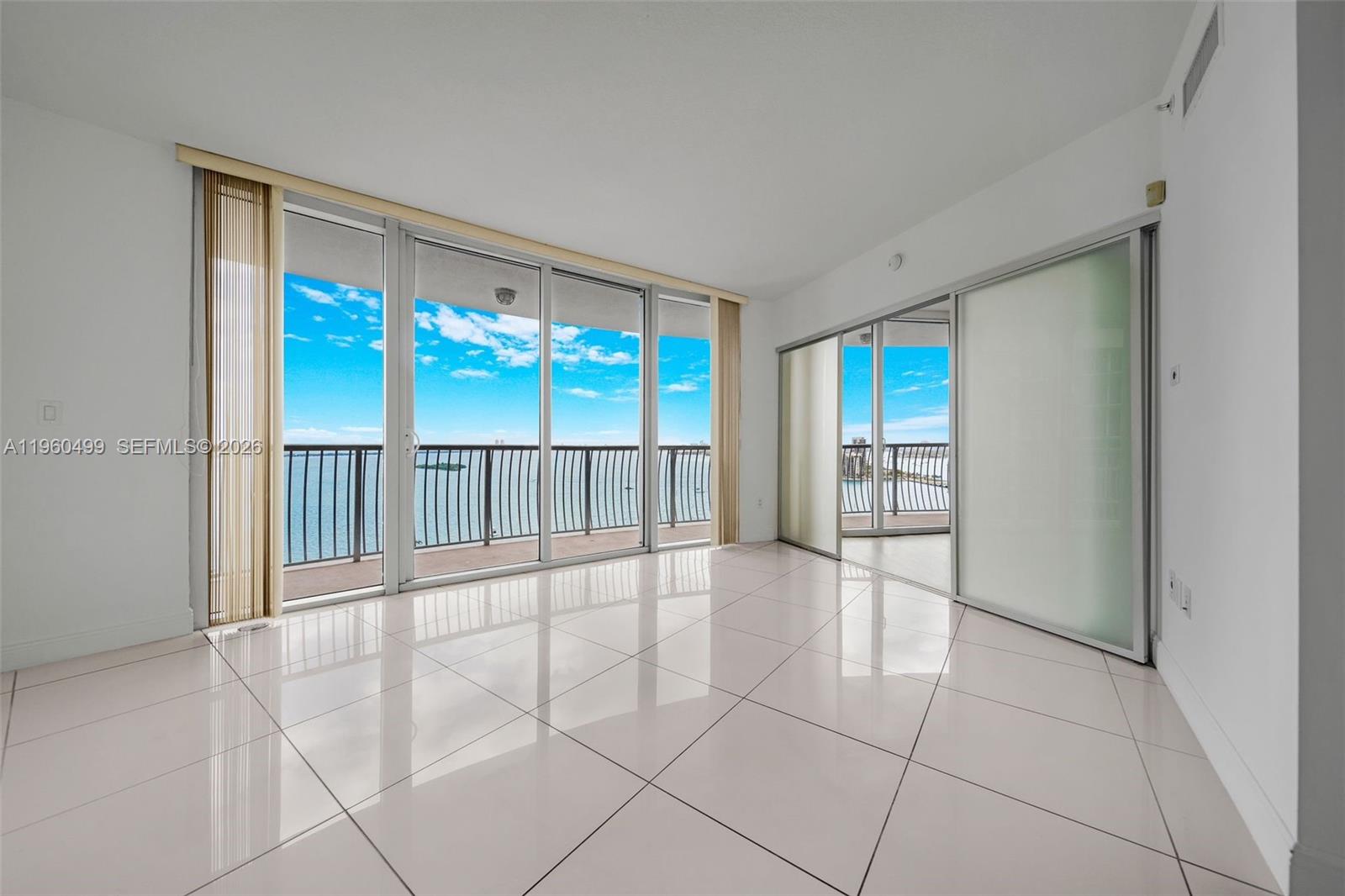 An empty room with white tile floors features large sliding glass doors opening to balconies — 1750 N Bayshore Dr # 2001, Miami FL 33132, MIAMI, FL