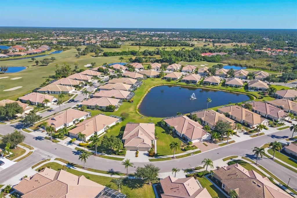 An aerial view shows a residential neighborhood with houses surrounding a central pond — 4820 WHISPERING OAKS DRIVE, NORTH PORT, FL