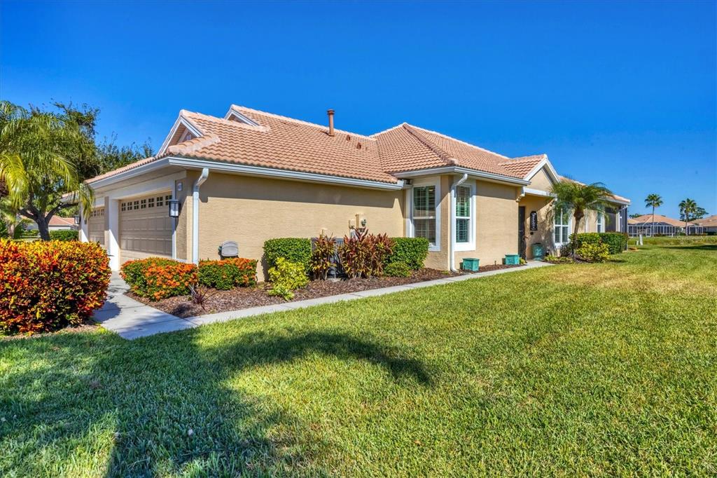 A tan stucco house with a tile roof and a garage sits on a lawn — 4820 WHISPERING OAKS DRIVE, NORTH PORT, FL