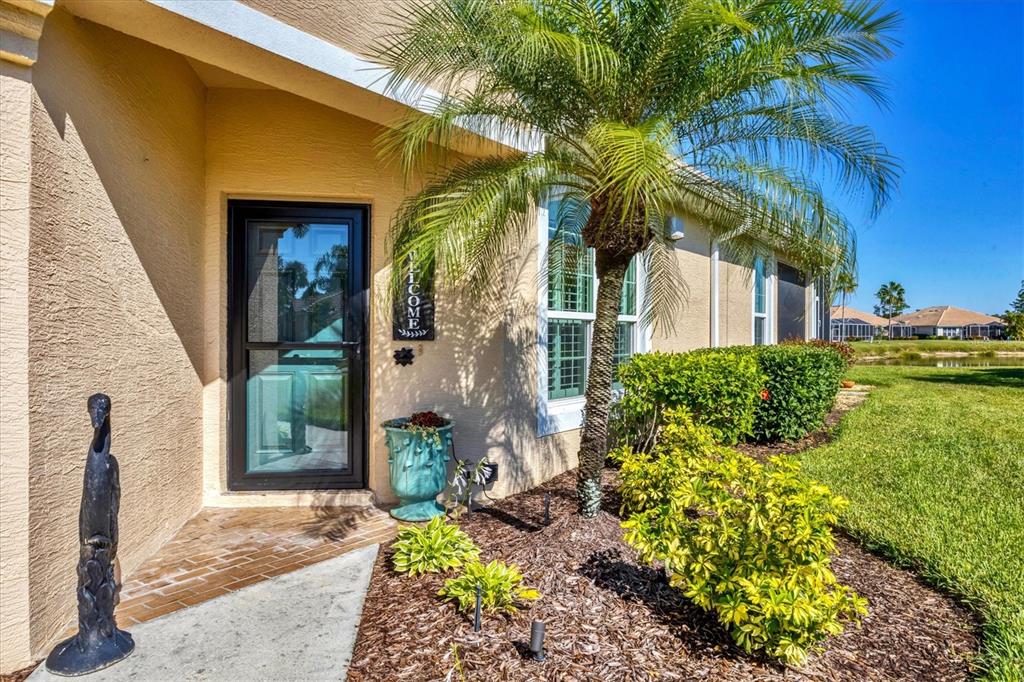 A palm tree stands next to a house entrance with a glass storm door — 4820 WHISPERING OAKS DRIVE, NORTH PORT, FL