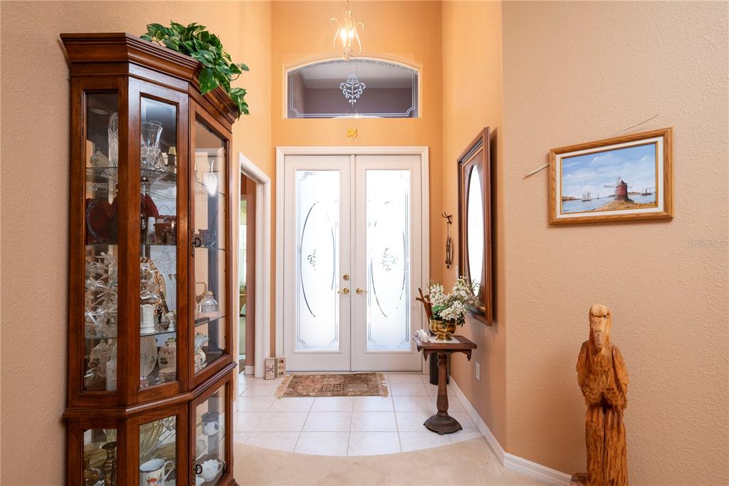 An entryway features a tall wooden display cabinet, a small pedestal table, and double glass doors — 10488 PRINCESS COURT, PUNTA GORDA, FL