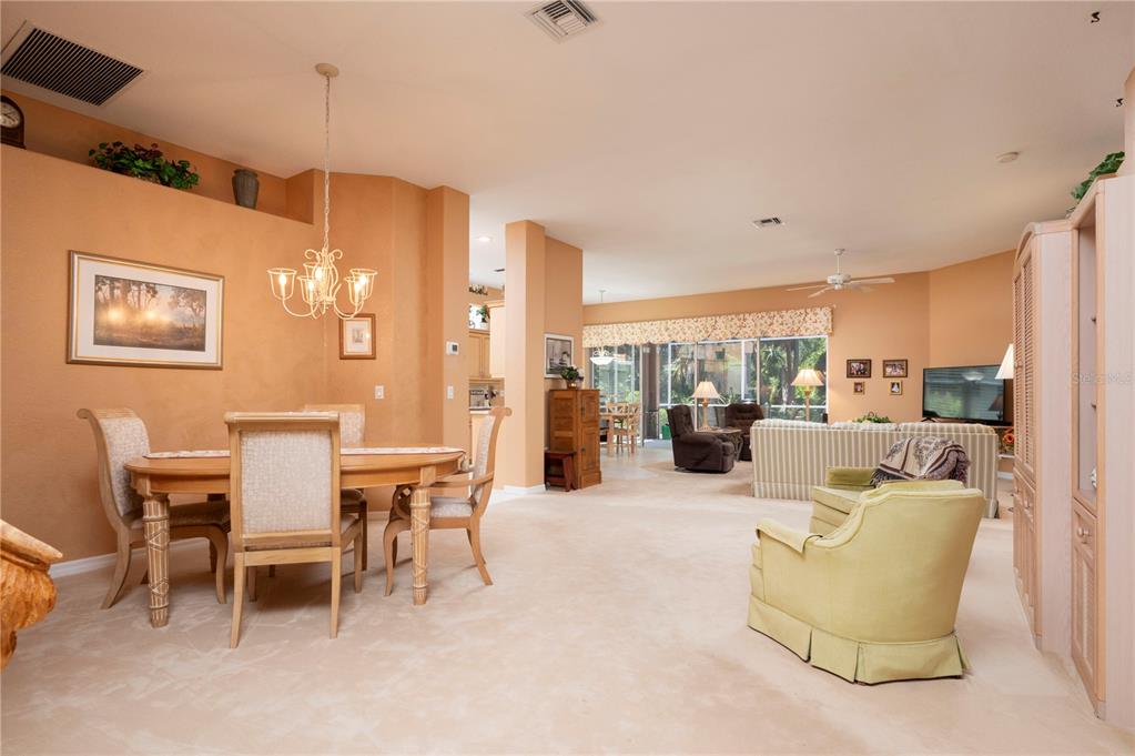 An open-concept living and dining area features beige carpeting, tan walls, and a chandelier — 10488 PRINCESS COURT, PUNTA GORDA, FL