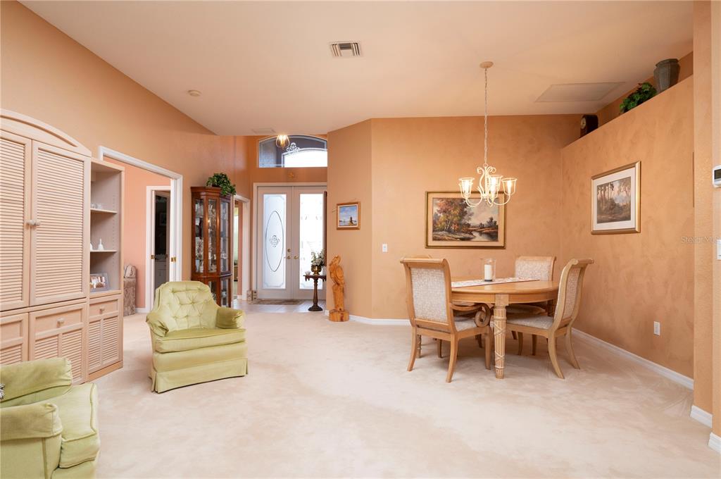A dining area and living space with beige carpet, peach walls, and a wooden table — 10488 PRINCESS COURT, PUNTA GORDA, FL