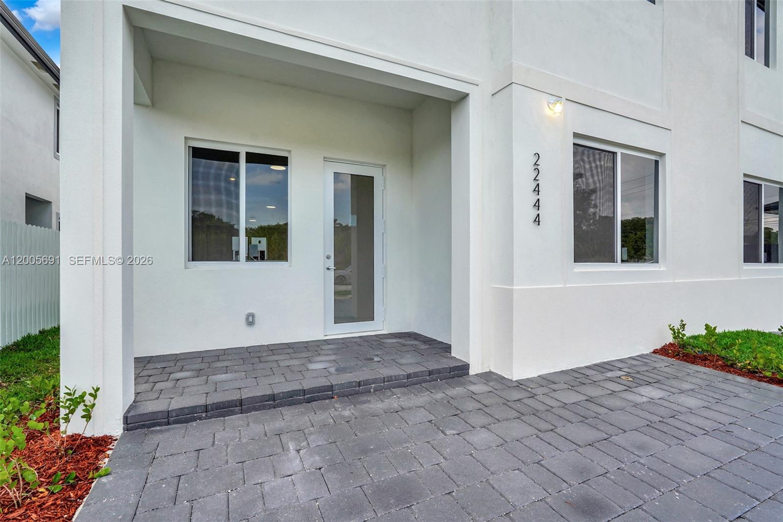 The exterior of a white building features a paved patio, a glass-paneled door, and windows — 22555 SW 125th Ave, Miami FL 33170, MIAMI, FL