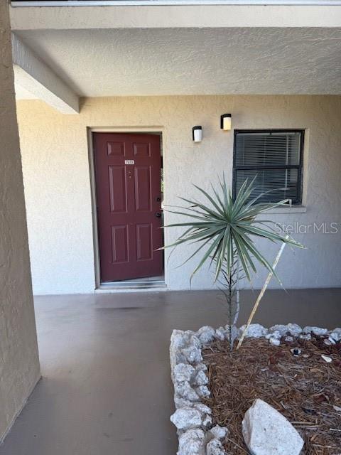 A red front door sits next to a window and a small plant in mulch — 7273 CLOISTER DRIVE UNIT 121, SARASOTA, FL