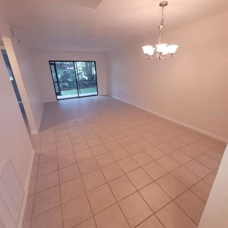 An empty dining area with beige tile flooring, a chandelier, and sliding glass doors — 7273 CLOISTER DRIVE UNIT 121, SARASOTA, FL