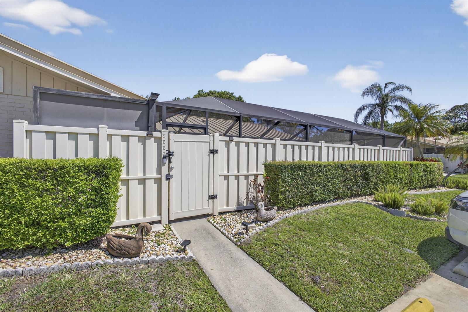 A white vinyl fence with a gate encloses a backyard pool area with a screen — 5662 Golden Eagle Circle, Palm Beach Gardens FL 33418, PALM BEACH GARDENS, FL