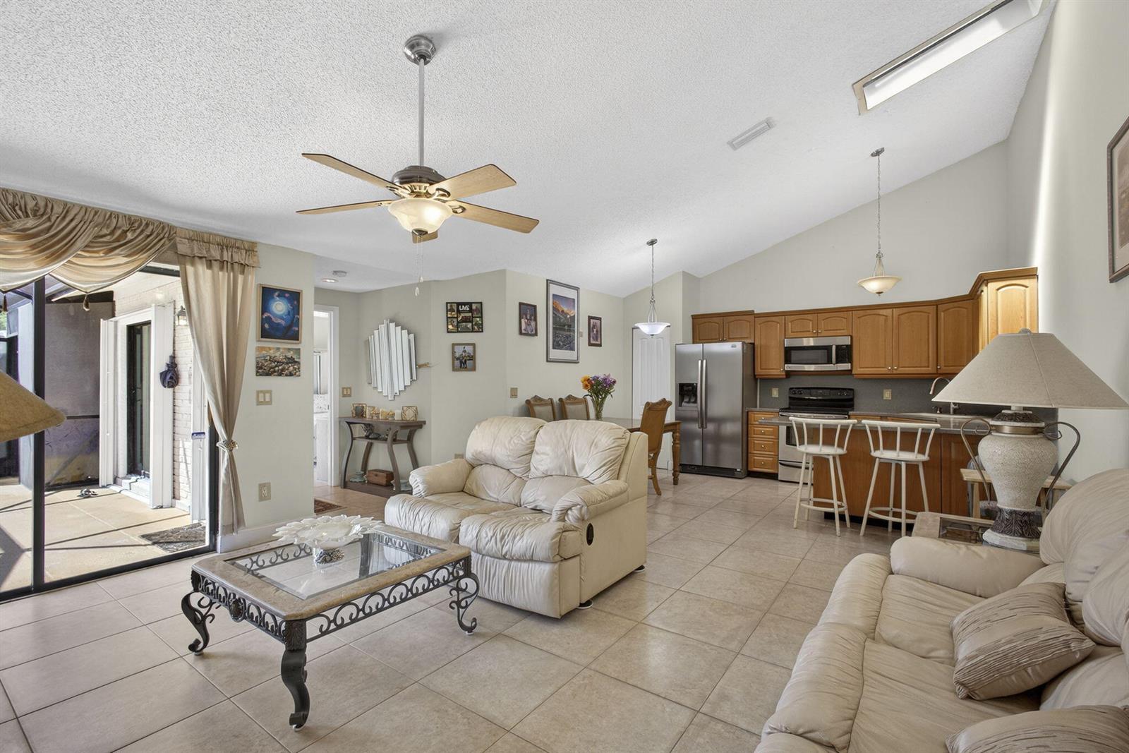 An open-concept living room and kitchen featuring tile floors, vaulted ceilings, and light-colored furniture — 5662 Golden Eagle Circle, Palm Beach Gardens FL 33418, PALM BEACH GARDENS, FL
