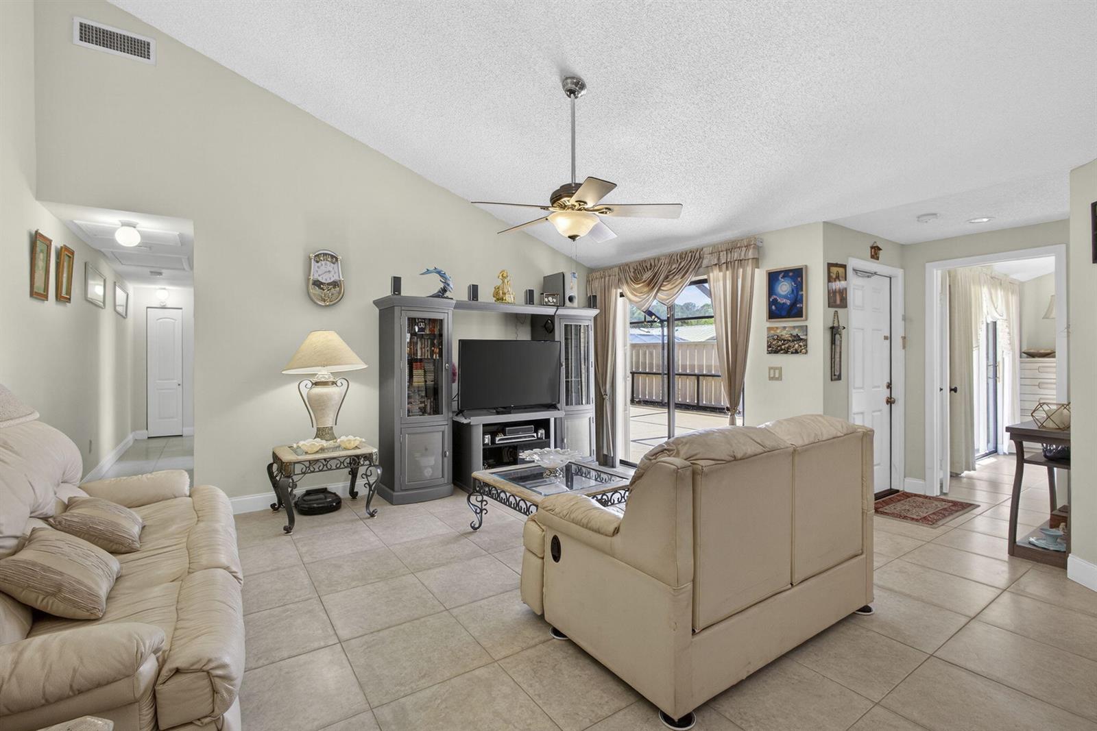 A living room features beige tile floors, a vaulted ceiling, and a beige leather sofa — 5662 Golden Eagle Circle, Palm Beach Gardens FL 33418, PALM BEACH GARDENS, FL