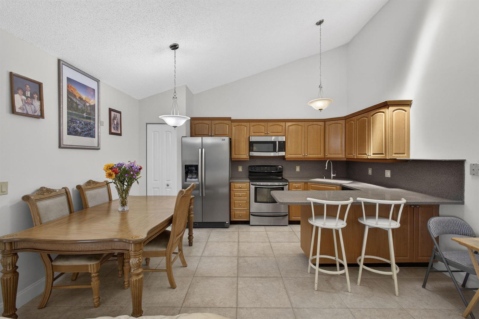 A kitchen and dining area with wood cabinets, stainless steel appliances, and tile flooring — 5662 Golden Eagle Circle, Palm Beach Gardens FL 33418, PALM BEACH GARDENS, FL