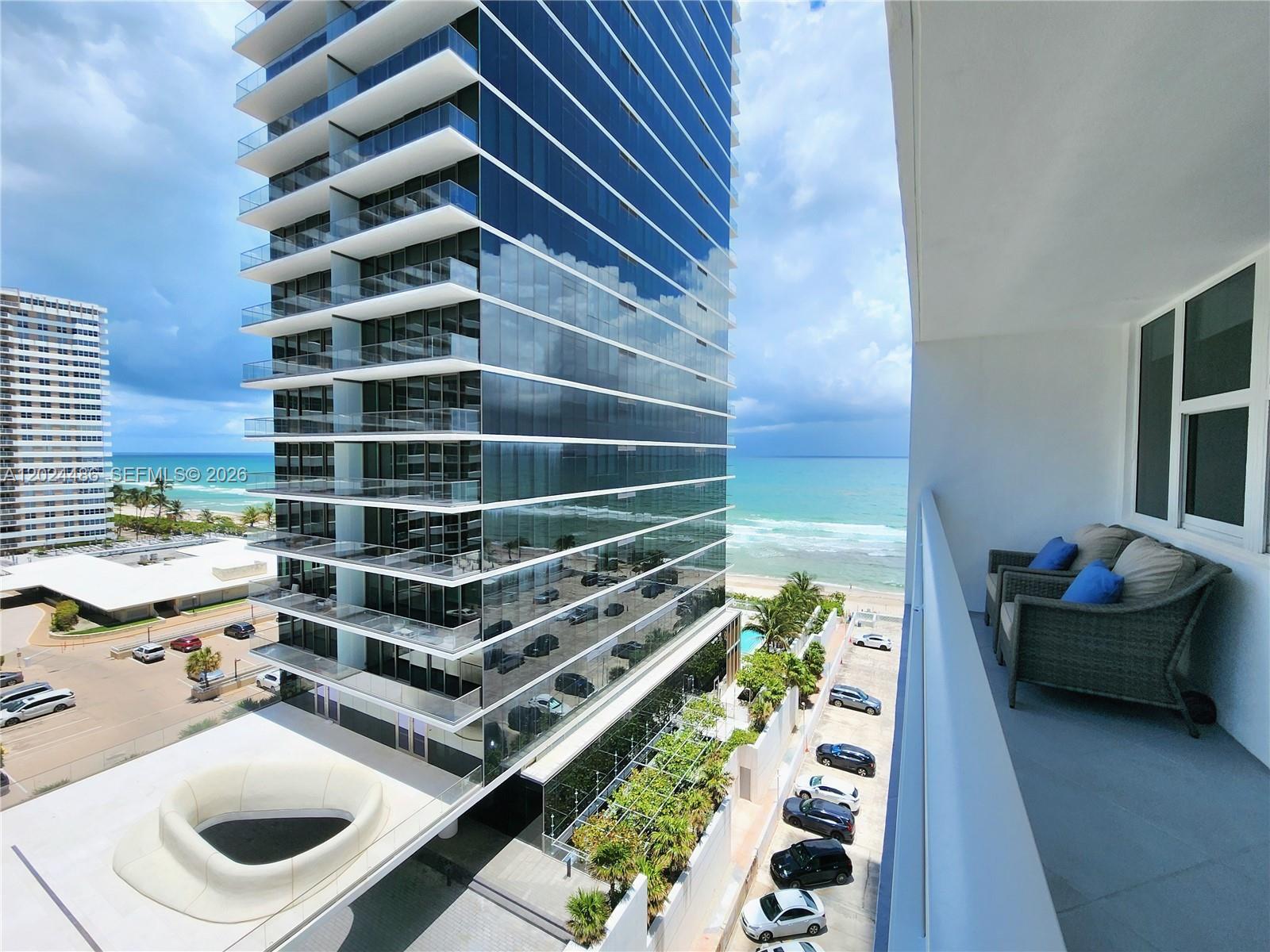 A balcony with two chairs overlooks a modern glass skyscraper and the ocean — 2030 S Ocean Dr # 923, Hallandale Beach FL 33009, HALLANDALE BEACH, FL