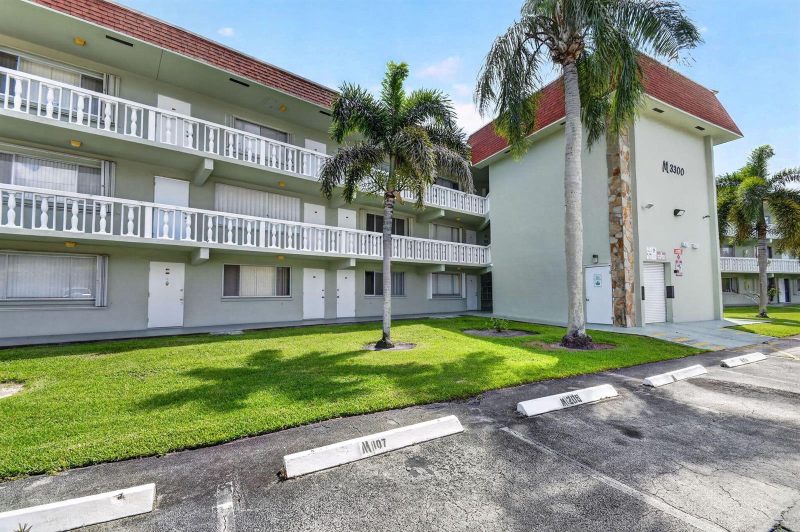 A three-story apartment building features white railings, palm trees, and a paved parking lot — 3300 Springdale Boulevard # 208, Palm Springs FL 33461, PALM SPRINGS, FL