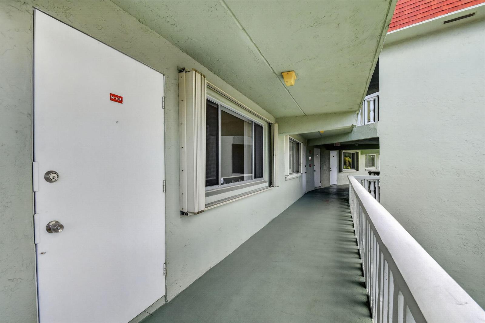 A three-story apartment building with a red roof, white balconies, and a paved parking lot — 3300 Springdale Boulevard # 208, Palm Springs FL 33461, PALM SPRINGS, FL