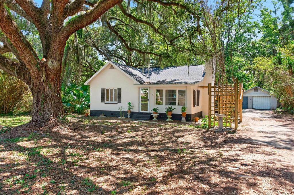 A single-story white house with a dark roof sits under a large oak tree — 112 N LAKE AVENUE, LEESBURG, FL