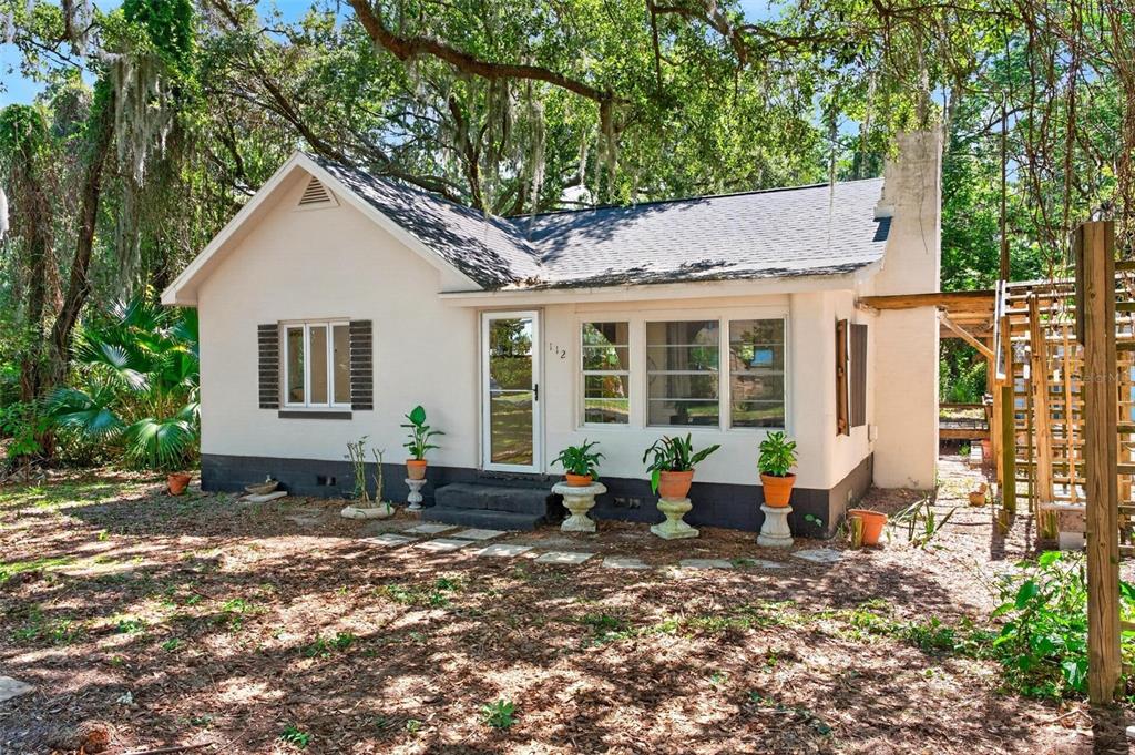 A single-story house with a white exterior, dark trim, and a front porch with potted plants — 112 N LAKE AVENUE, LEESBURG, FL