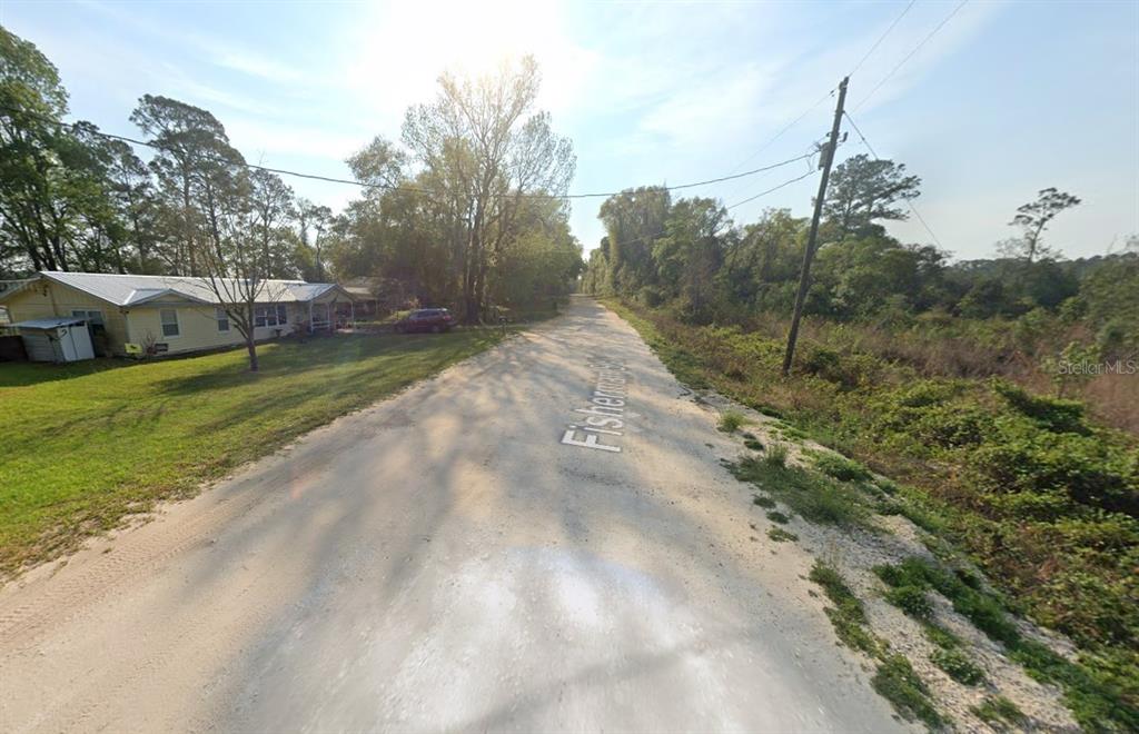 A dirt road runs past a yellow house with a metal roof and trees — 129 FISHERMANS DRIVE, INTERLACHEN, FL
