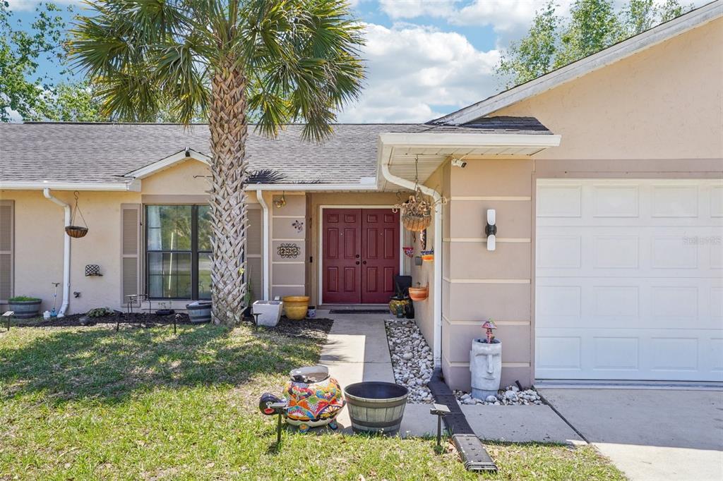 A single-story house exterior features a tan stucco facade, red double front doors, and a palm tree — 236 MARION OAKS LANE, OCALA, FL