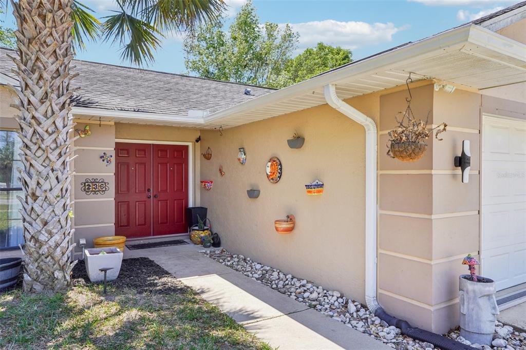 The exterior of a beige house features a red double door and decorative wall planters — 236 MARION OAKS LANE, OCALA, FL