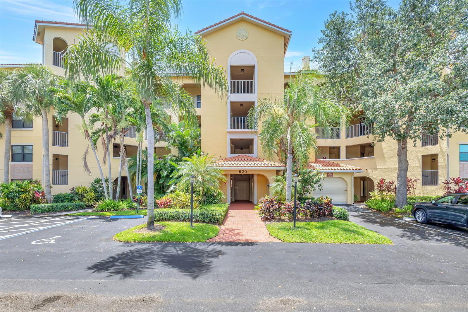 A multi-story yellow apartment building features a central entrance with a tiled roof — 800 Uno Lago Drive # 302, Juno Beach FL 33408, JUNO BEACH, FL