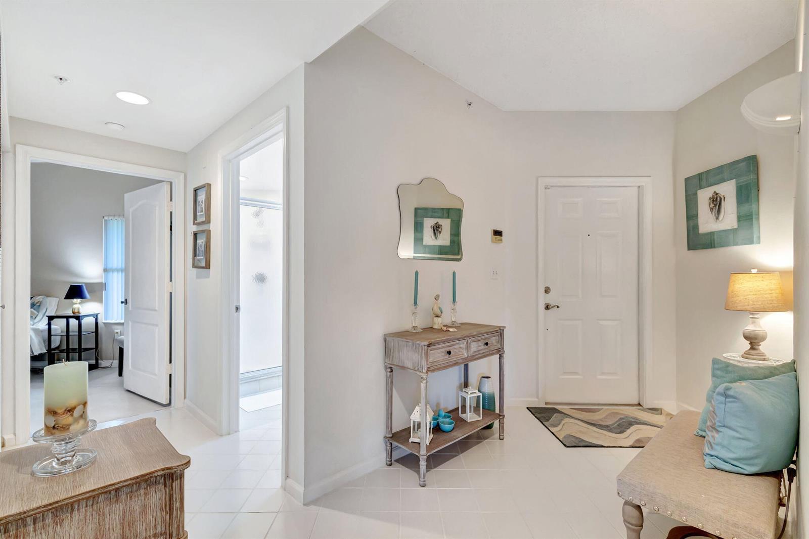 A bright entryway features white tile floors, a console table, and a bench with pillows — 800 Uno Lago Drive # 302, Juno Beach FL 33408, JUNO BEACH, FL