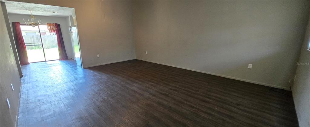 An empty living room features dark wood-look flooring, gray walls, and a sliding glass door — 2021 BUCKEYE ROAD NE, WINTER HAVEN, FL