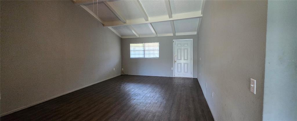 An empty living room features dark wood-look flooring, gray walls, and a vaulted beamed ceiling — 2021 BUCKEYE ROAD NE, WINTER HAVEN, FL