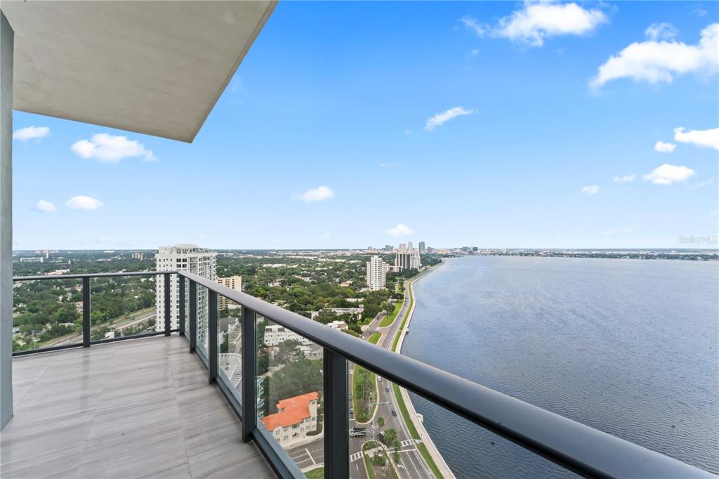 A high-rise balcony with glass railings overlooks a coastal road and a large body of water — 3101 BAYSHORE BOULEVARD UNIT 2501, TAMPA, FL