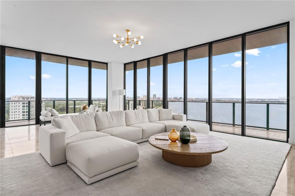 A living room features a white sectional sofa, a round wooden coffee table, and floor-to-ceiling windows — 3101 BAYSHORE BOULEVARD UNIT 2501, TAMPA, FL