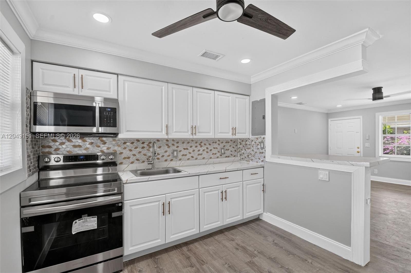 A kitchen features white cabinets, stainless steel appliances, a patterned backsplash, and wood-look flooring — 824 Bayberry Dr, Lake Park FL 33403, LAKE PARK, FL